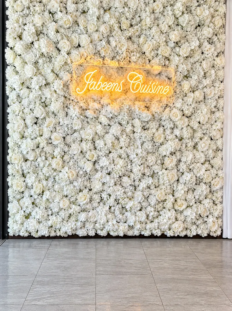 Mur de roses blanches avec l'enseigne lumineuse Jabeen's Cuisine